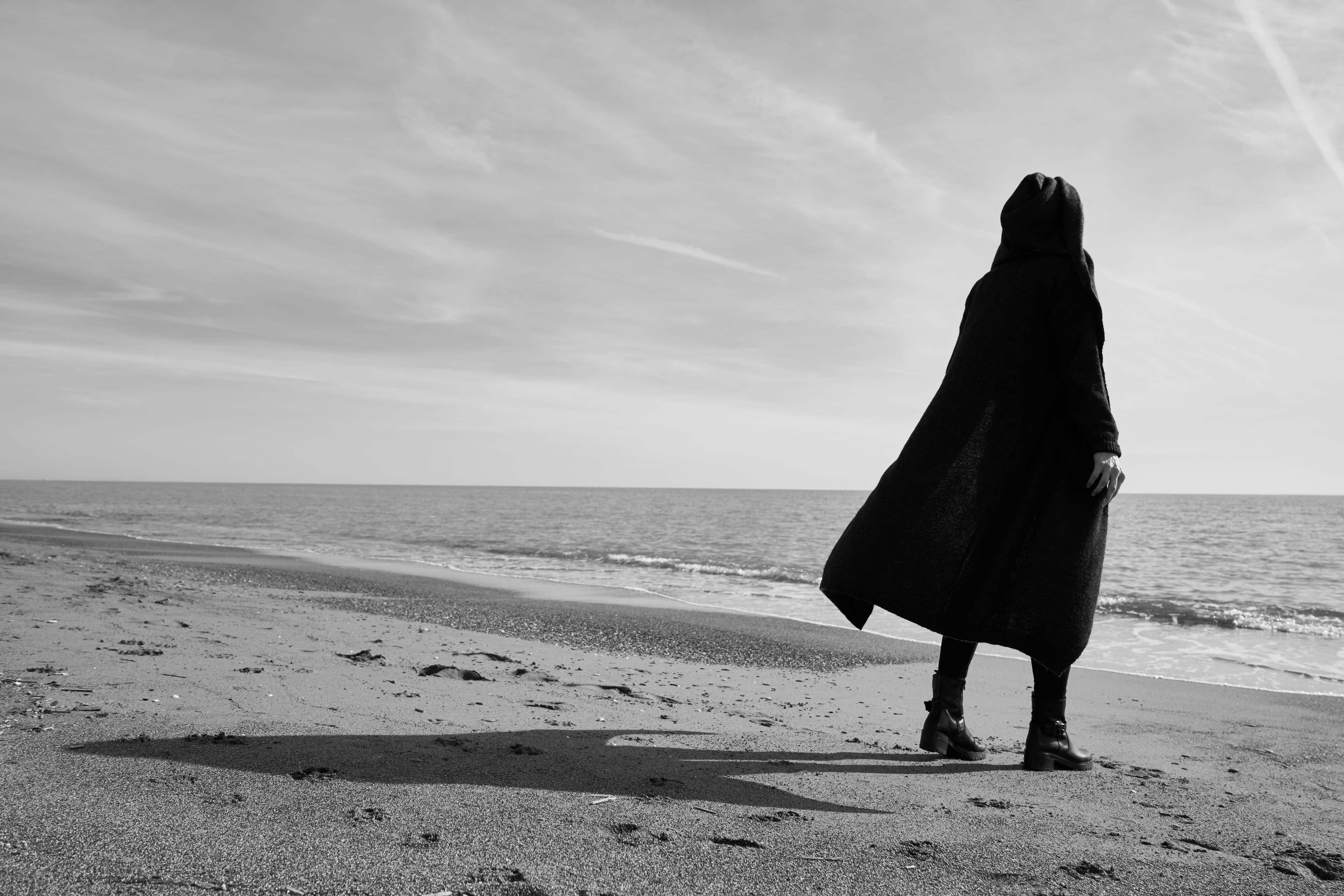 Eine Frau mit dunklem Mantel steht am Strand
