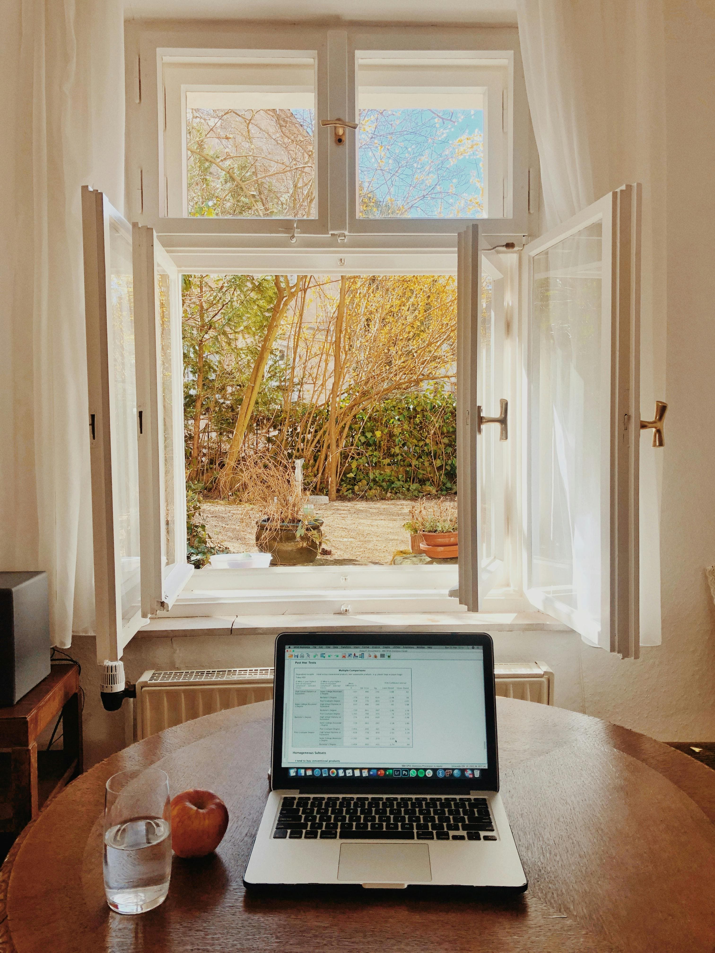 Szene mit Laptop auf Tisch mit Blick in den grünen Garten durch offenes Fenster.