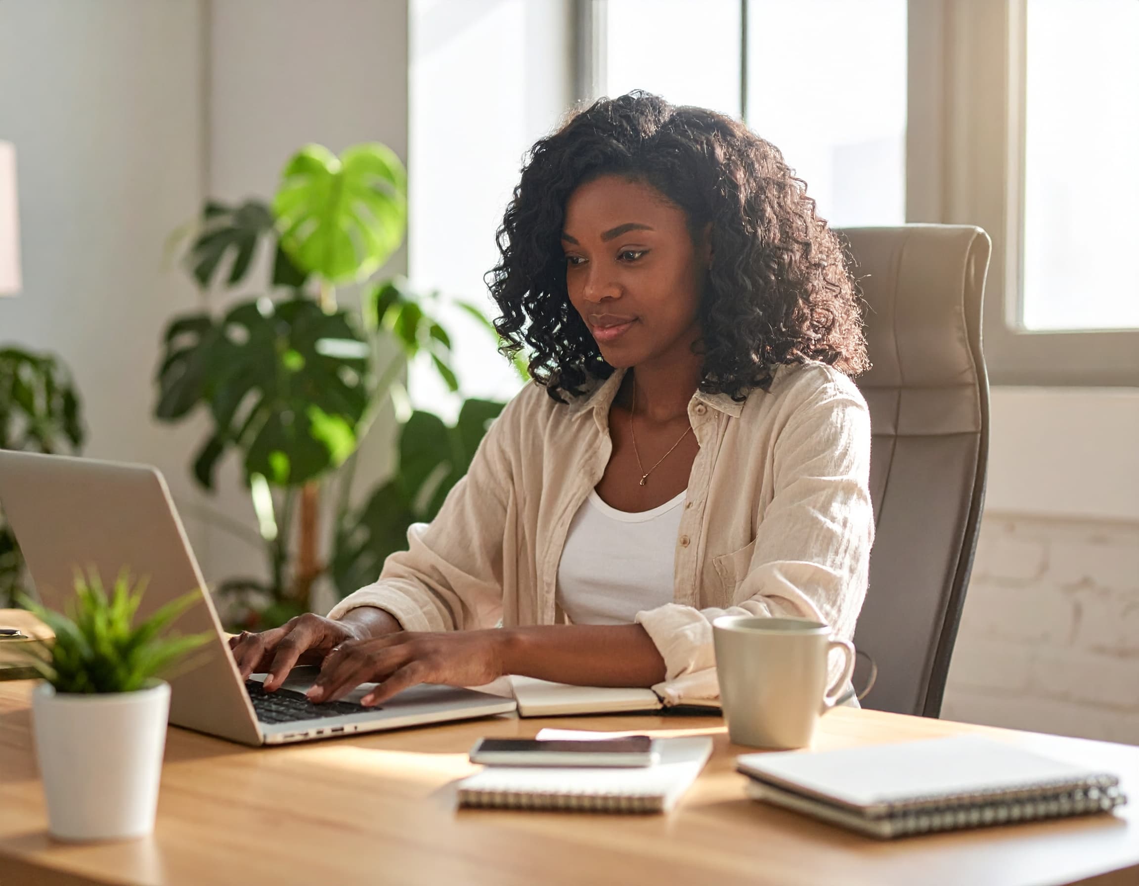 Eine Frau sitzt an einem aufgeräumten Arbeitsplatz und arbeitet konzentriert an ihrem Laptop.