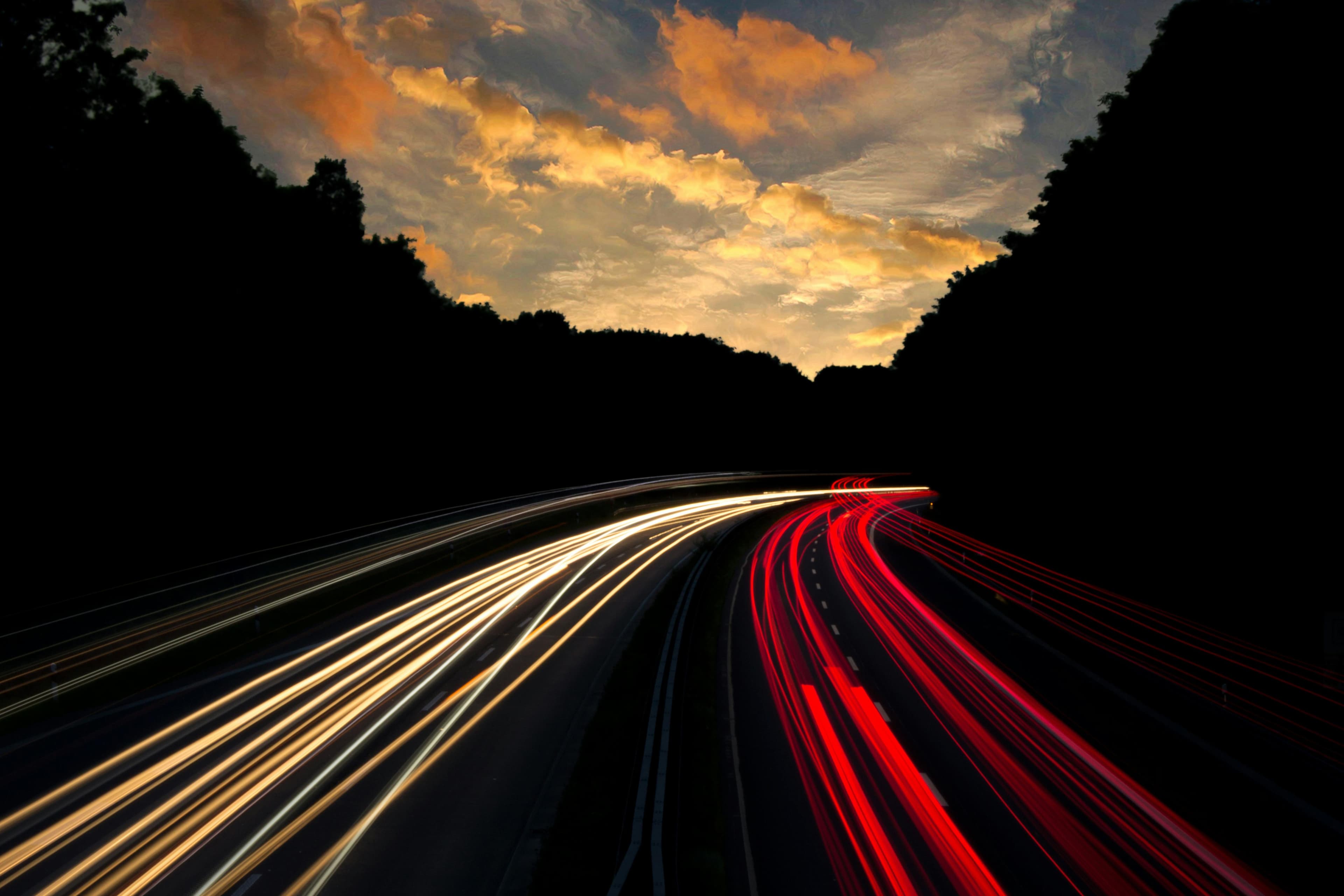 Foto von einer Autobahnbrücke herunter mit Langzeitbelichtung. Die Lichter werden zu langen weißen und roten Bahnen.