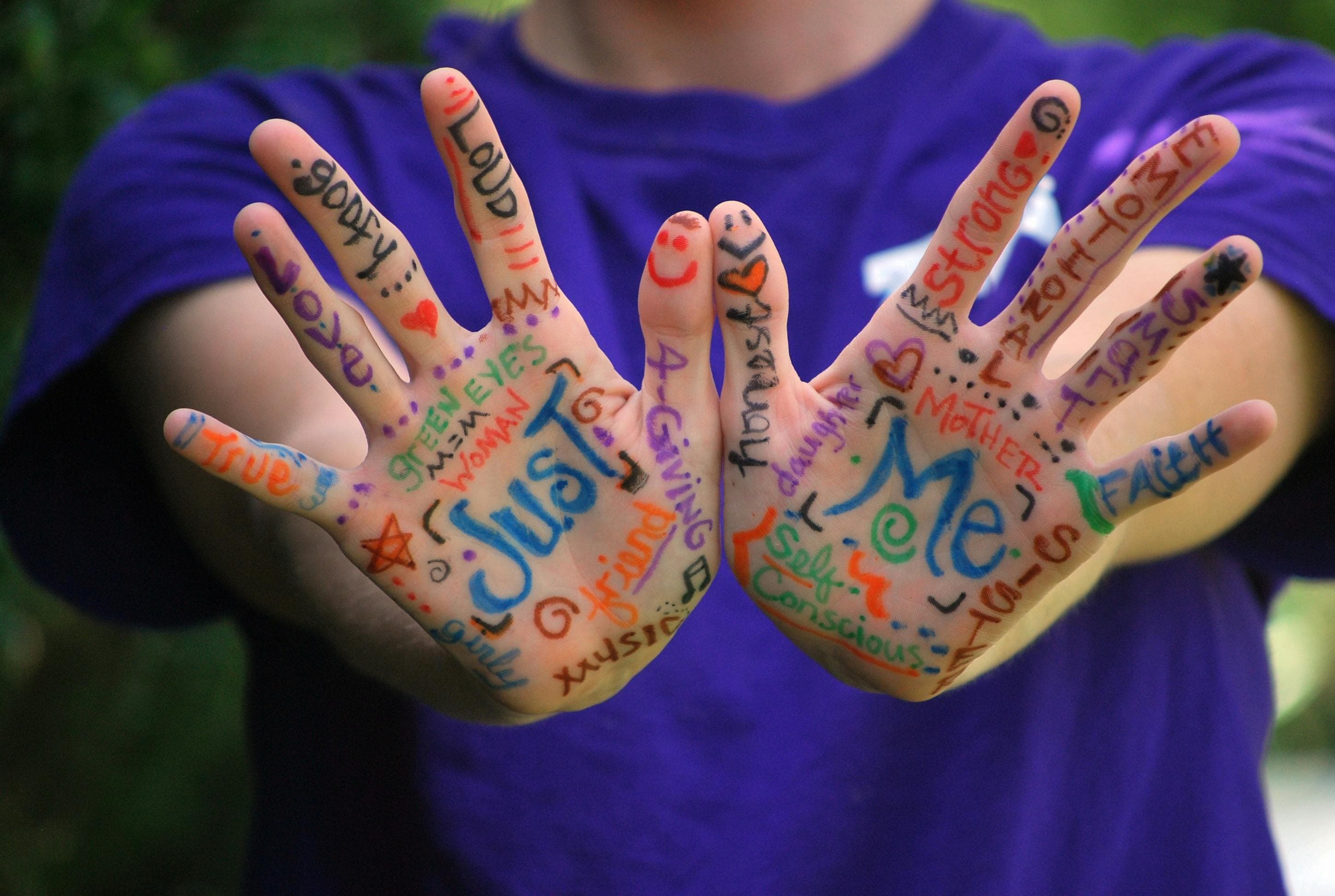 Zwei geöffnete Handflächen, bunt beschriftet mit Wörtern wie ‚Just Me‘, ‚strong‘, ‚loud‘ und ‚love‘